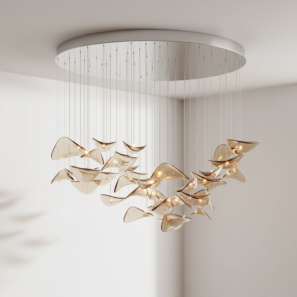 Round brushed-metal canopy with amber glass leaves on cables, hung in a pale room, from this Clérachic pendant light.