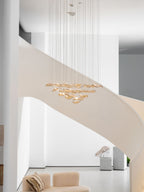 Tall white stairwell with a pale curving stair, where a Clérachic amber leaf pendant hangs high above a sofa and a plinth.