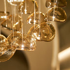 Close view of rounded amber glass leaves lit from within, each hung on its own cable, from this Clérachic pendant.