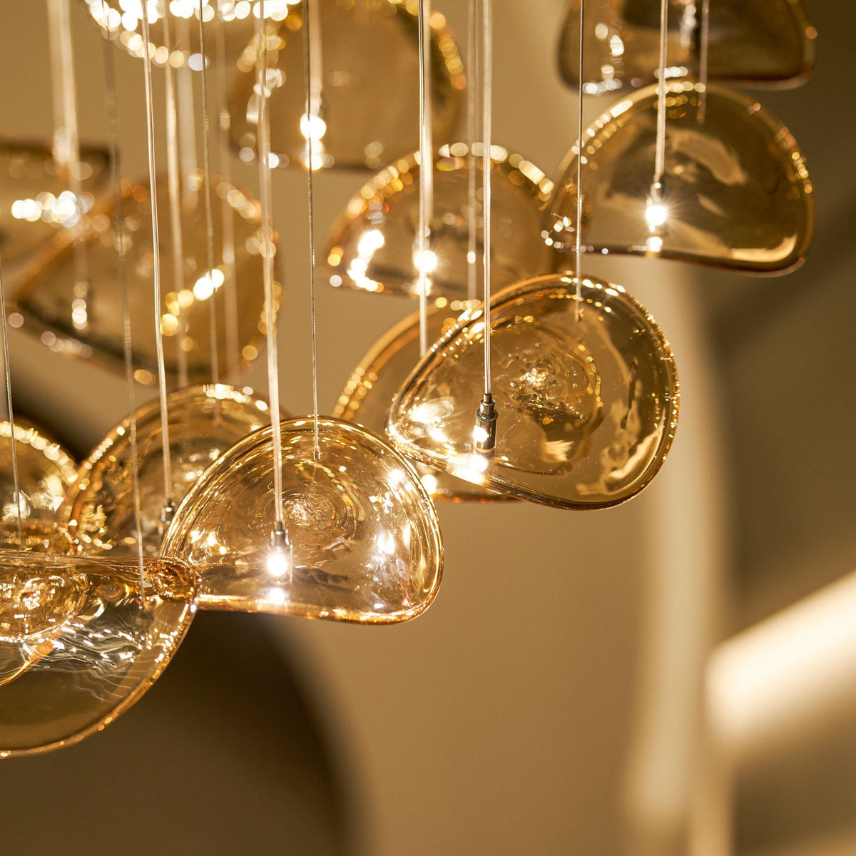 Close view of rounded amber glass leaves lit from within, each hung on its own cable, from this Clérachic pendant.