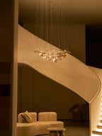 Warm-lit stairwell with a cream curved stair, where a small Clérachic amber leaf pendant hangs above a seat and cushion.