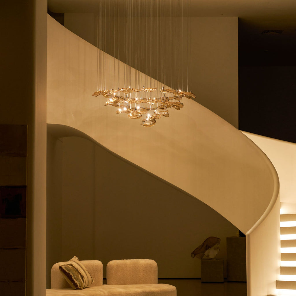 Amber leaf pendant from Clérachic glowing in a dim stairwell, with a sofa and cushion at the lower left.