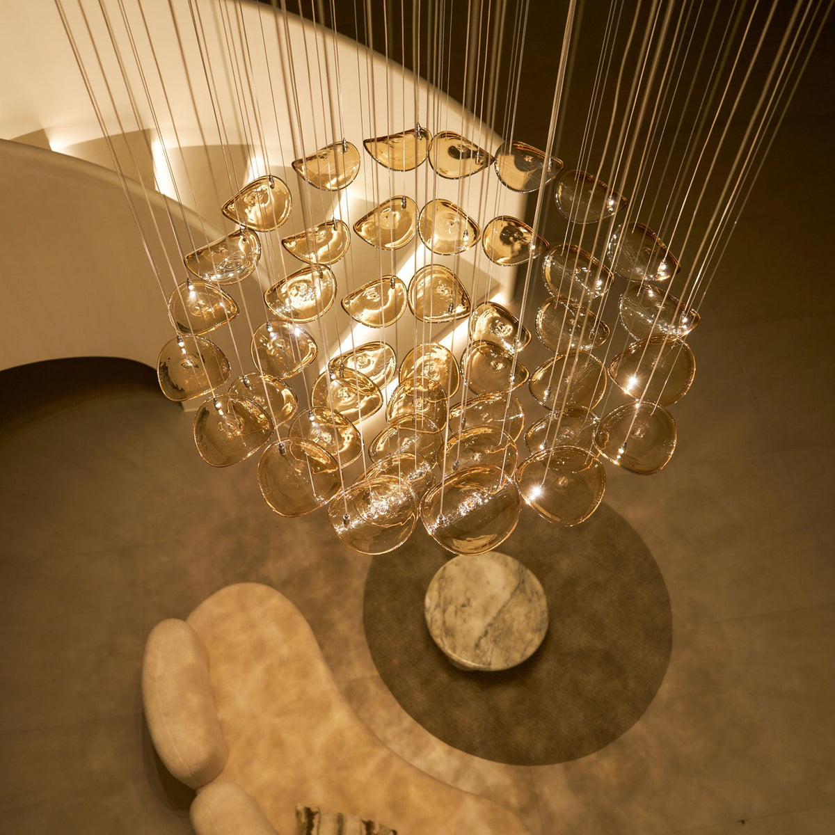 Looking up at a Clérachic pendant of amber glass leaves, hung in layered rings on long cables above a round table.