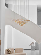 Bright white stairwell with a curved stair, where a Clérachic amber leaf pendant hangs well above a cream sofa.