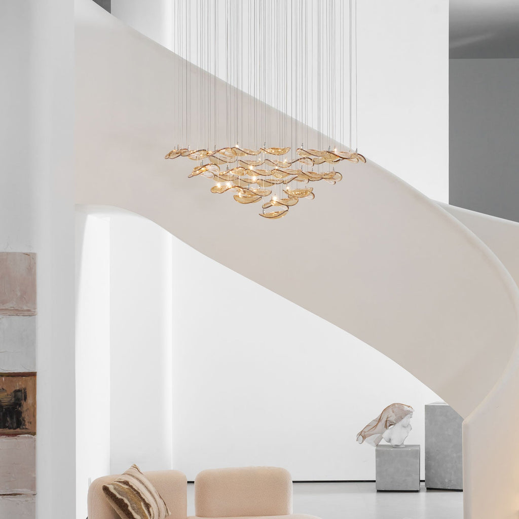 Pale stairwell with a Clérachic amber glass leaf pendant hanging in layers above a cream sofa and a stone plinth.