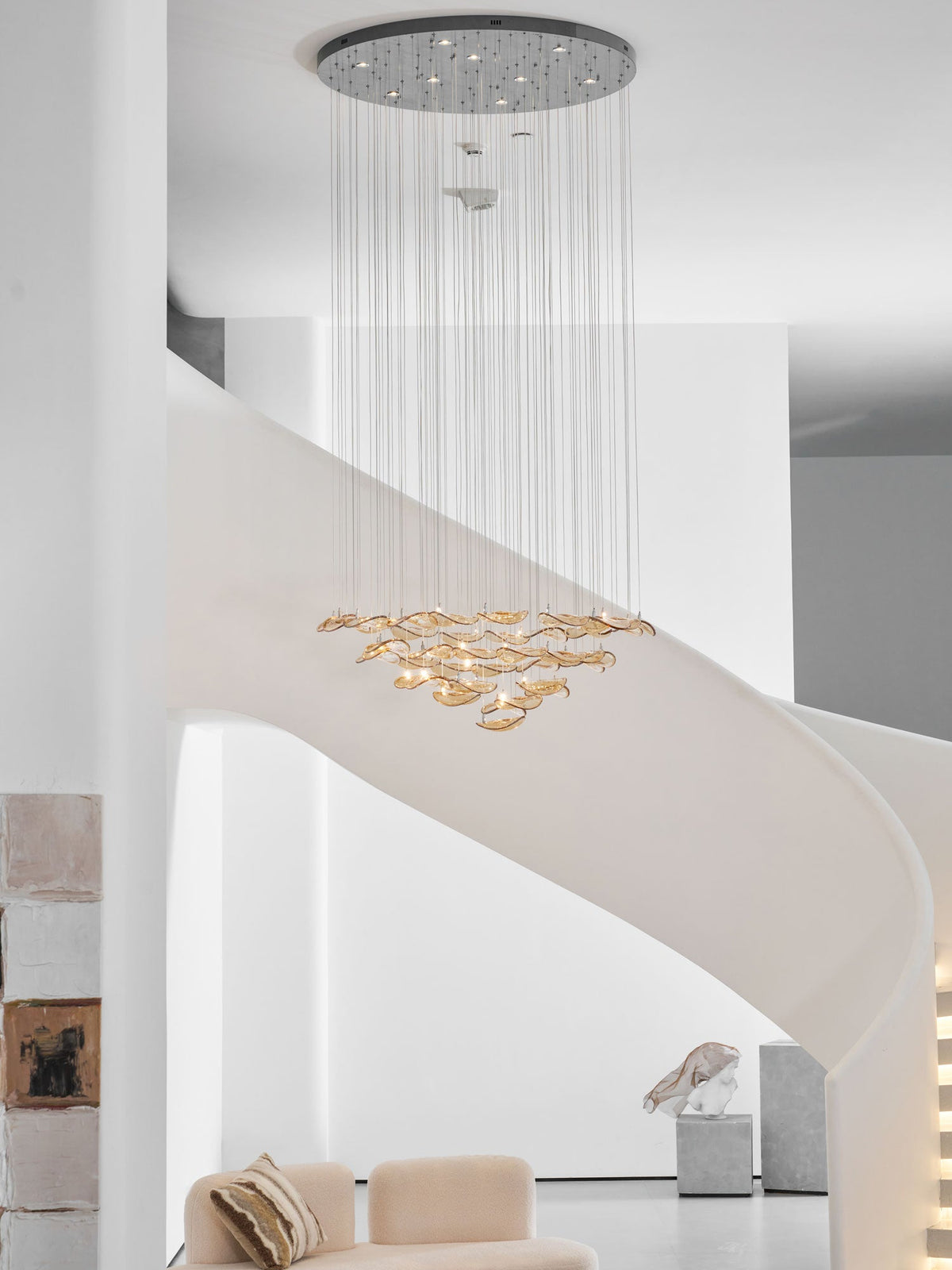 Clérachic amber leaf pendant with a round chrome canopy high above, hung in a white stairwell beside a stone sculpture.