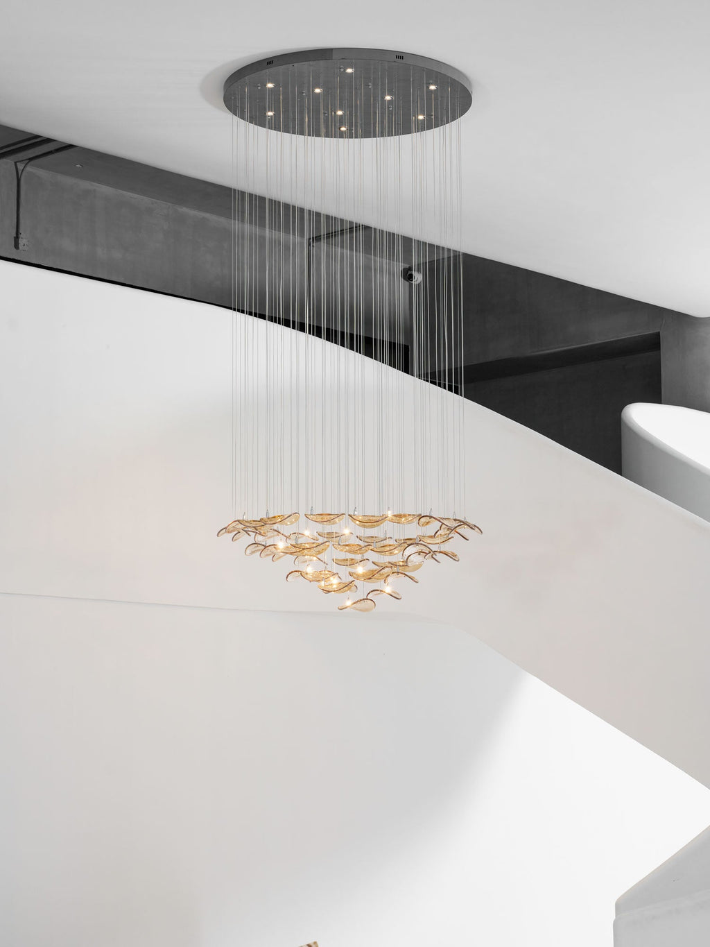 Pendant from Clérachic with a dark round canopy and a long cable drop, its amber glass leaves hung in rings below a white stair.