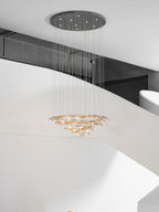 Pendant from Clérachic with a dark round canopy and a long cable drop, its amber glass leaves hung in rings below a white stair.