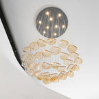 Tiered rings of rounded amber glass leaves hang in a lit ball shape, from this Clérachic pendant, below a dark round canopy.