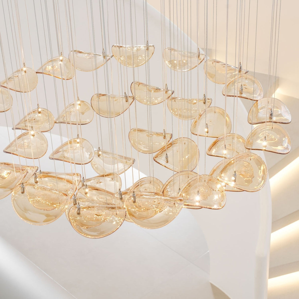Close view of tiers of amber glass leaves, each with a small metal clip, hung on cables in this Clérachic pendant.