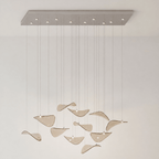 Rectangular chrome canopy with small lights and a small group of amber glass leaves on cables, on a cream wall, from Clérachic.