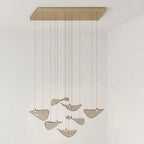 Gold rectangular canopy above a small group of tilted amber glass leaves on cables, in a pale room, from Clérachic.