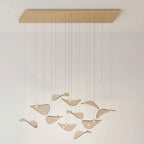 Brass-toned rectangular canopy and a few amber glass leaves, with soft leaf shadows on the pale wall, from Clérachic.