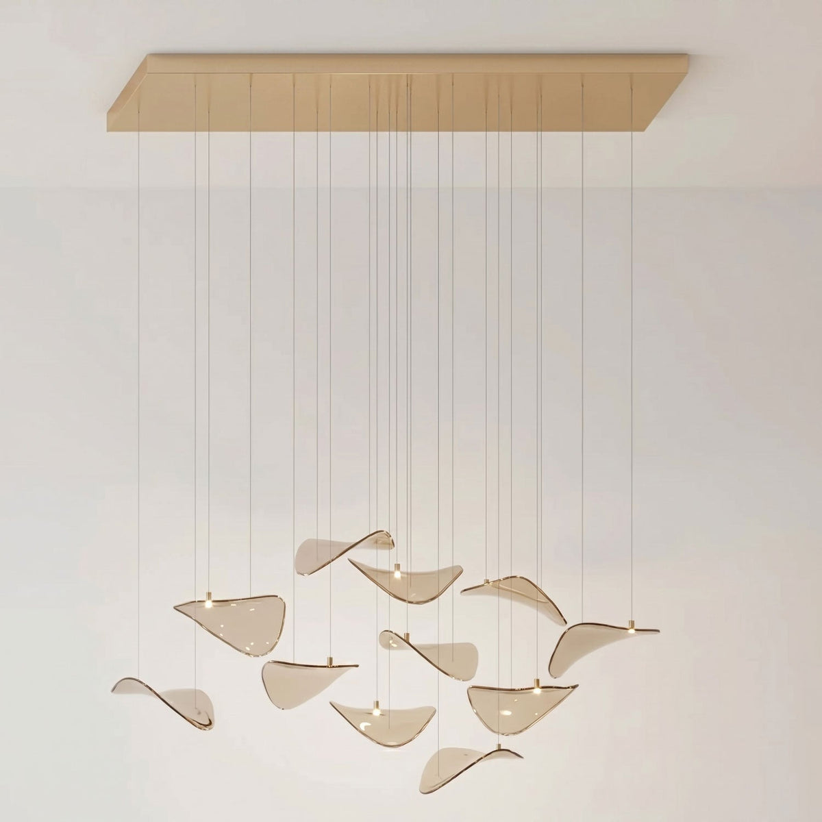 Brass-toned rectangular canopy and a few amber glass leaves, with soft leaf shadows on the pale wall, from Clérachic.