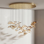 Round gold canopy over a wide, lit cluster of amber glass leaves, shown in a pale room with soft shadows, from Clérachic.