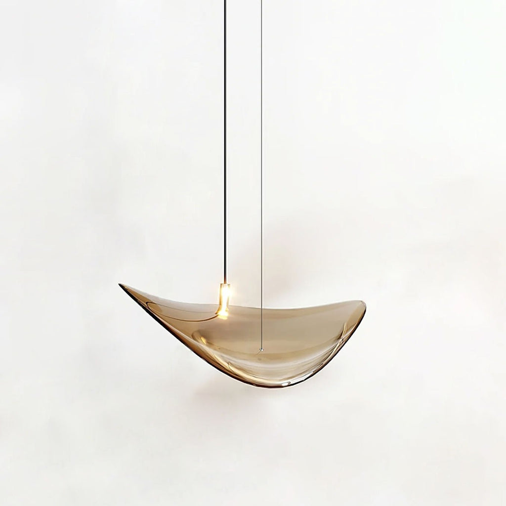 Single amber glass leaf with a small light on its upper face, hung on a dark cable, from this Clérachic pendant, on a white backdrop.