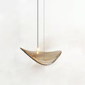 Single amber glass leaf with a small light on its upper face, hung on a dark cable, from this Clérachic pendant, on a white backdrop.