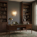 Clérachic glass-leaf wall light glowing above a wooden writing desk, between two dark bookcases and beside a brass desk lamp.