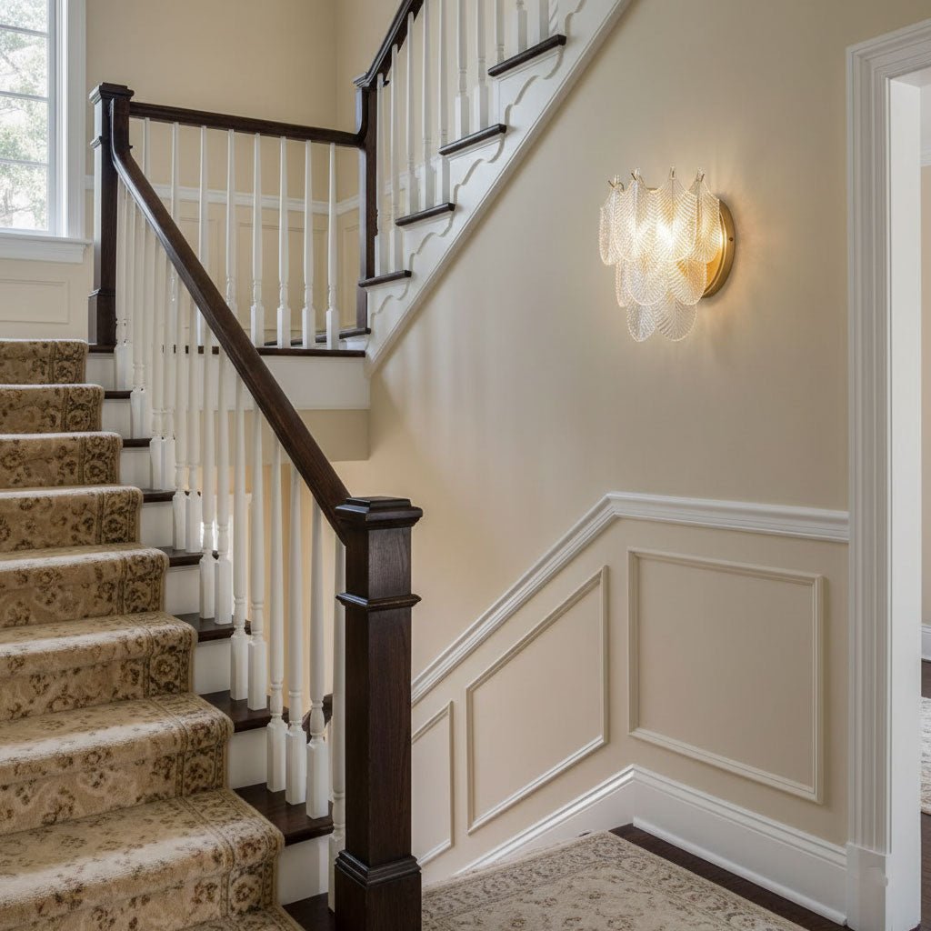 Clérachic wall light on a cream wall beside a staircase with a dark handrail, white balusters and a patterned stair carpet.