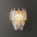 Close view of the lit Clérachic wall light on a dark grey wall, its tiers of clear ribbed glass leaves glowing warm at the centre.