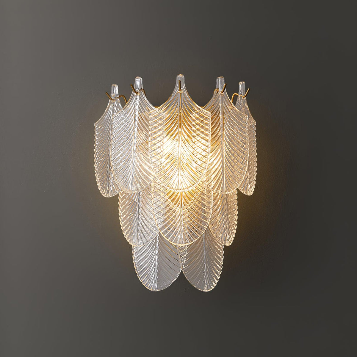 Close view of the lit Clérachic wall light on a dark grey wall, its tiers of clear ribbed glass leaves glowing warm at the centre.