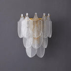 Front view of the unlit Clérachic wall light on a grey wall, three tiers of ribbed glass leaves with brass hooks along the top.