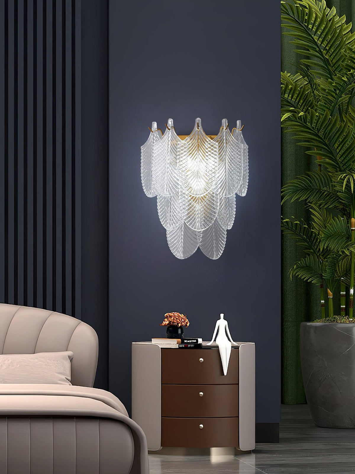 Clérachic glass-leaf wall light lit cool-white on a navy wall, above a bedside chest of drawers with a white figurine.