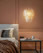 A Clérachic wall light glowing warm above a bed on a terracotta panelled wall, with a woven brown throw and a dark metal side table.