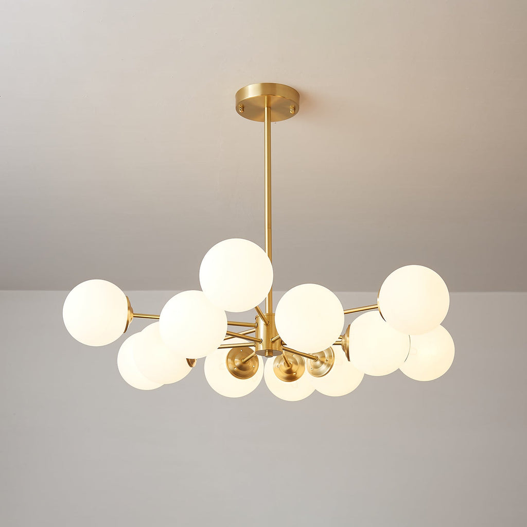 Glowing frosted orbs on slim brass arms, a Clérachic chandelier hung from a round brass canopy against a soft grey ceiling.