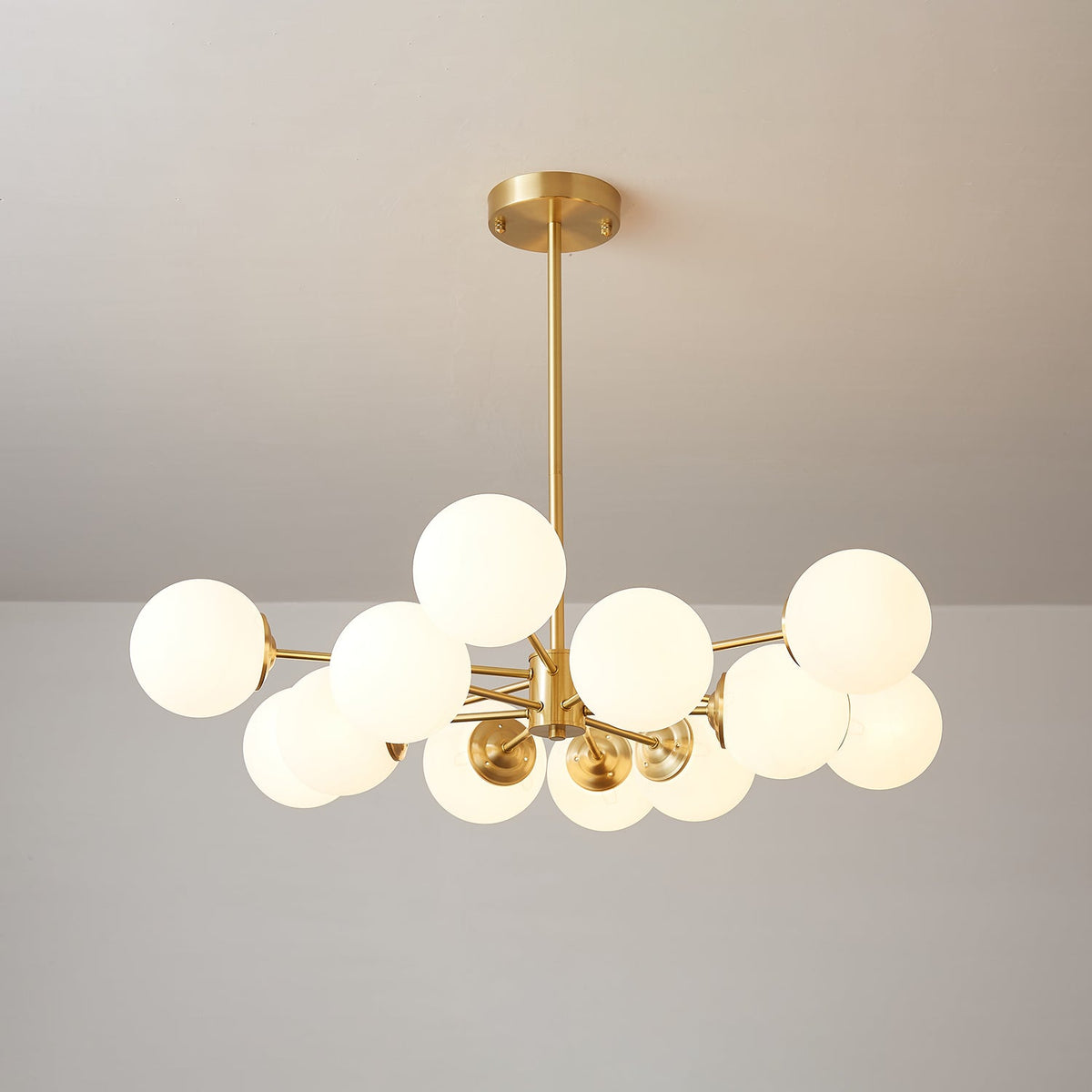 Glowing frosted orbs on slim brass arms, a Clérachic chandelier hung from a round brass canopy against a soft grey ceiling.