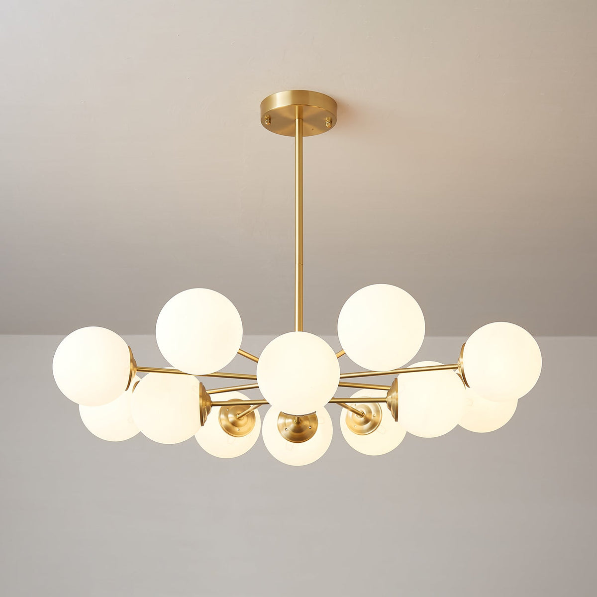Low, wide Clérachic chandelier with glowing white orbs fanned around a brass centre on a pale grey wall.