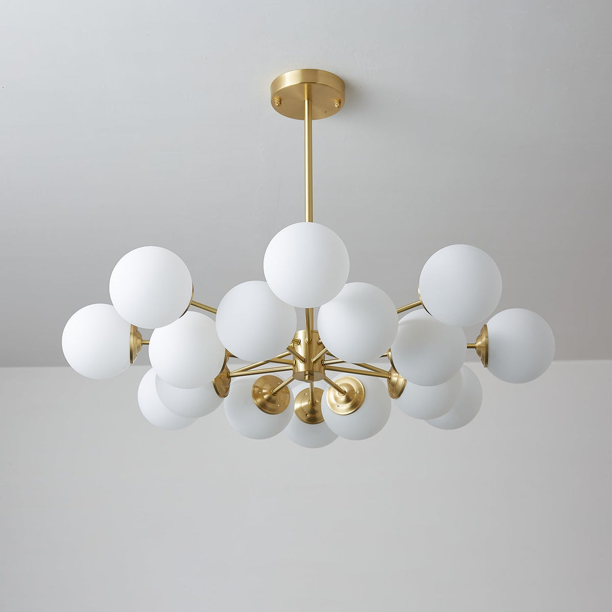 Unlit Clérachic chandelier with matt white glass orbs on brass arms, hung against a cool grey backdrop.
