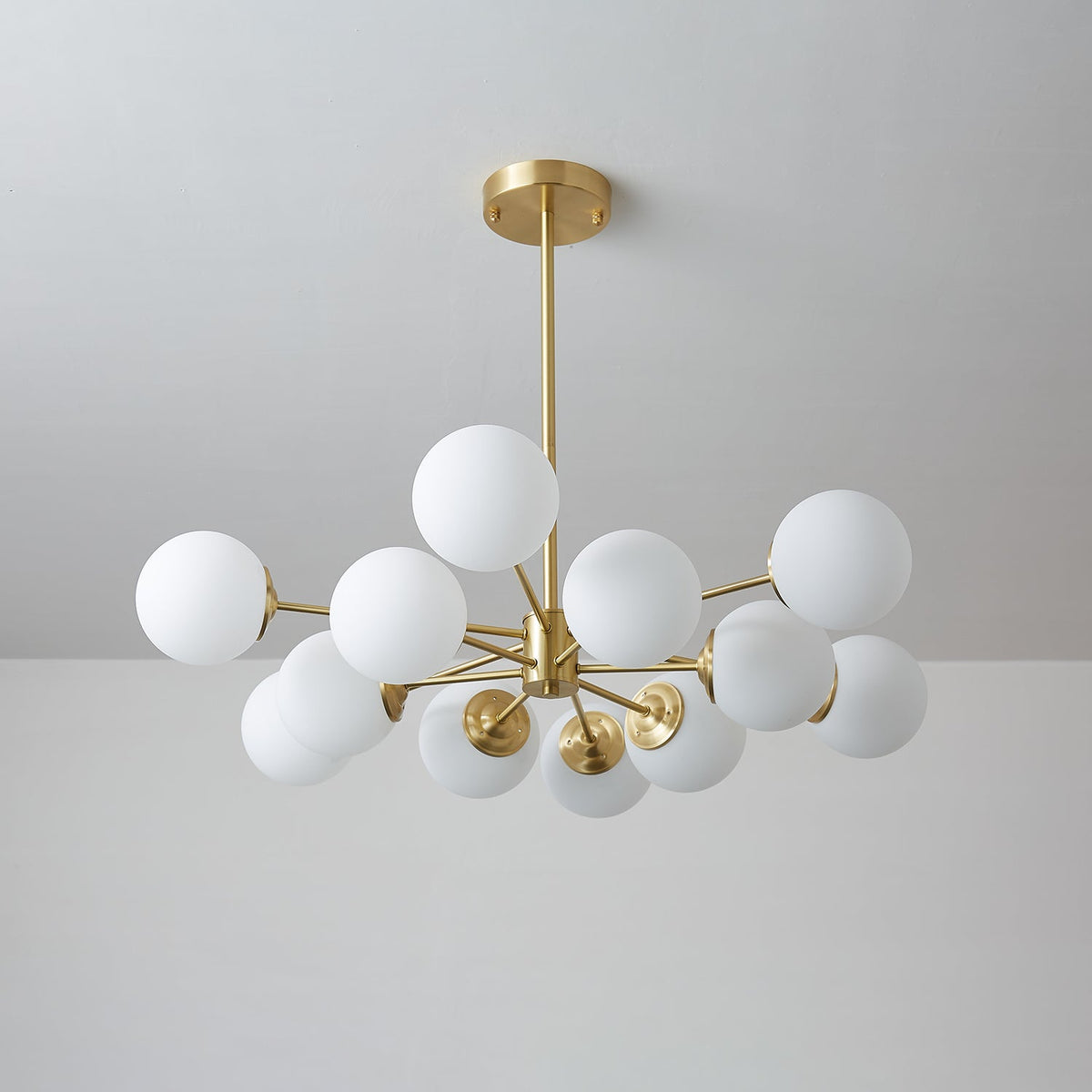 Cool-toned view of this Clérachic chandelier switched off, its white orbs clustered around a brass hub.