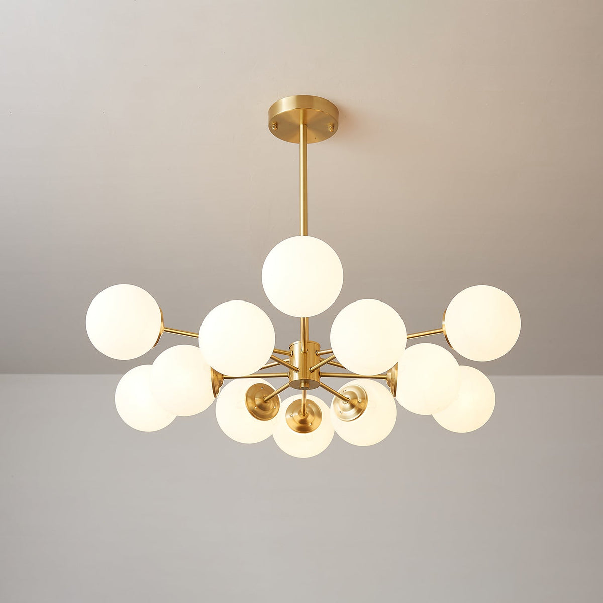 Clérachic chandelier lit with one orb on top and others fanned out below, on a soft beige-grey backdrop.