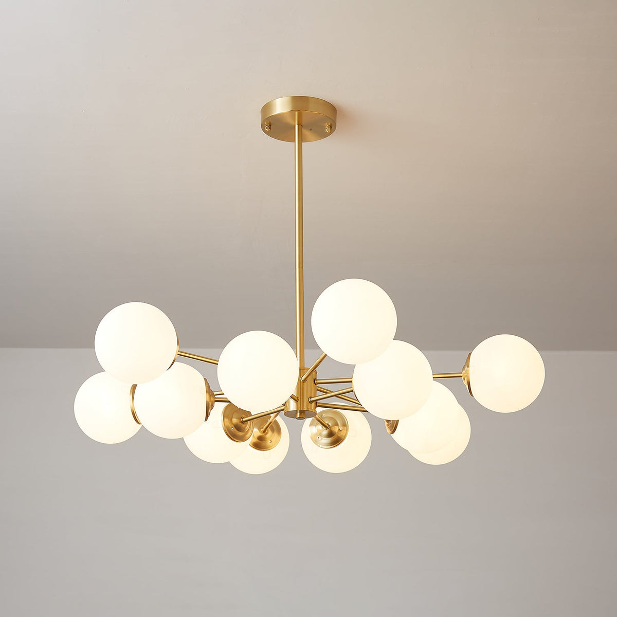 A Clérachic chandelier with lit white orbs, some tucked under the arms, hung from a slim brass rod.