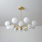 Unlit white orbs on slim brass arms, a Clérachic chandelier seen against a pale grey wall.
