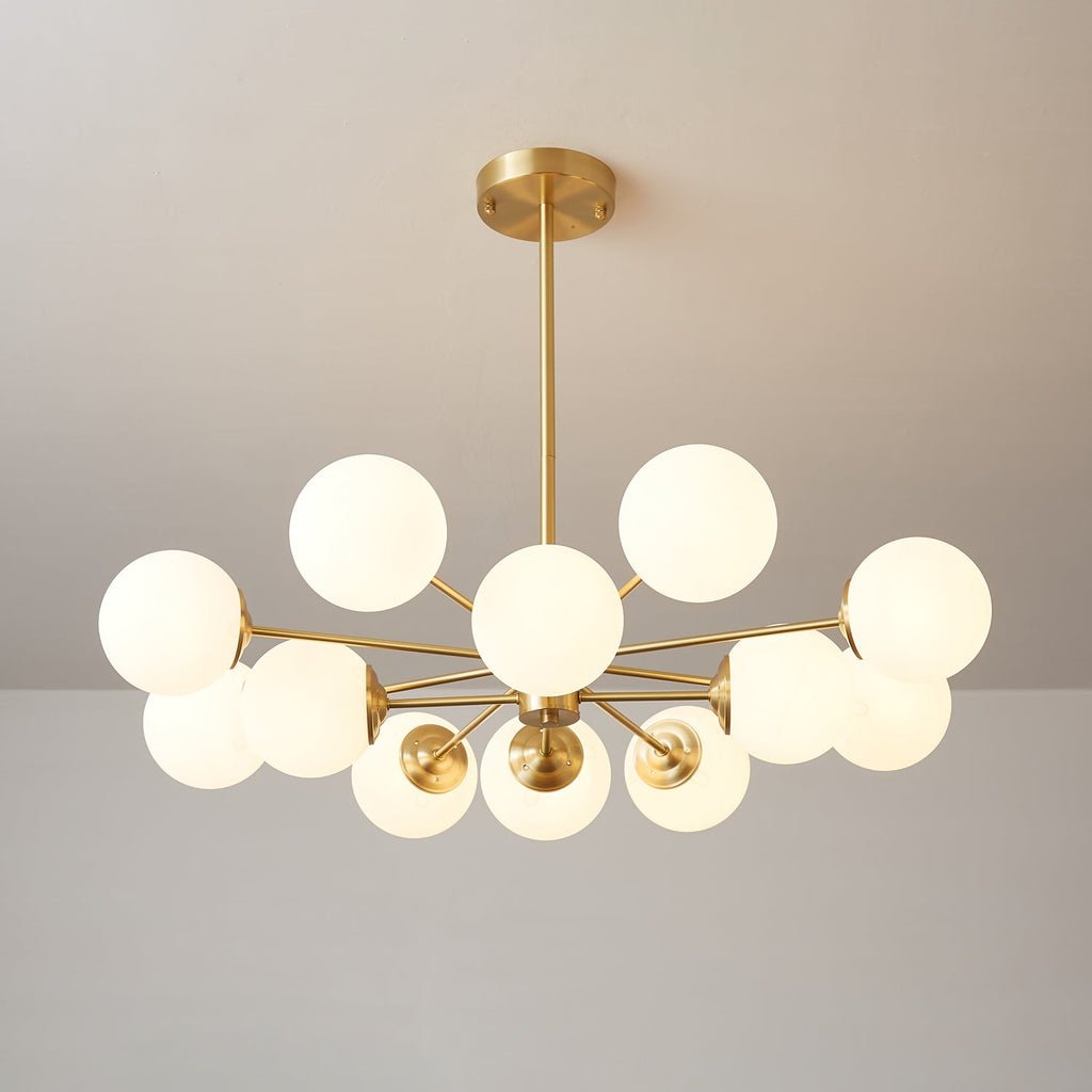 Clérachic chandelier with warm lit orbs on long brass arms, shown at a wide angle against a taupe wall.
