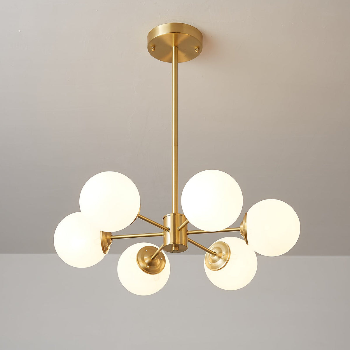 Smaller Clérachic chandelier with six lit white glass orbs around a brass hub, hung from a long rod.