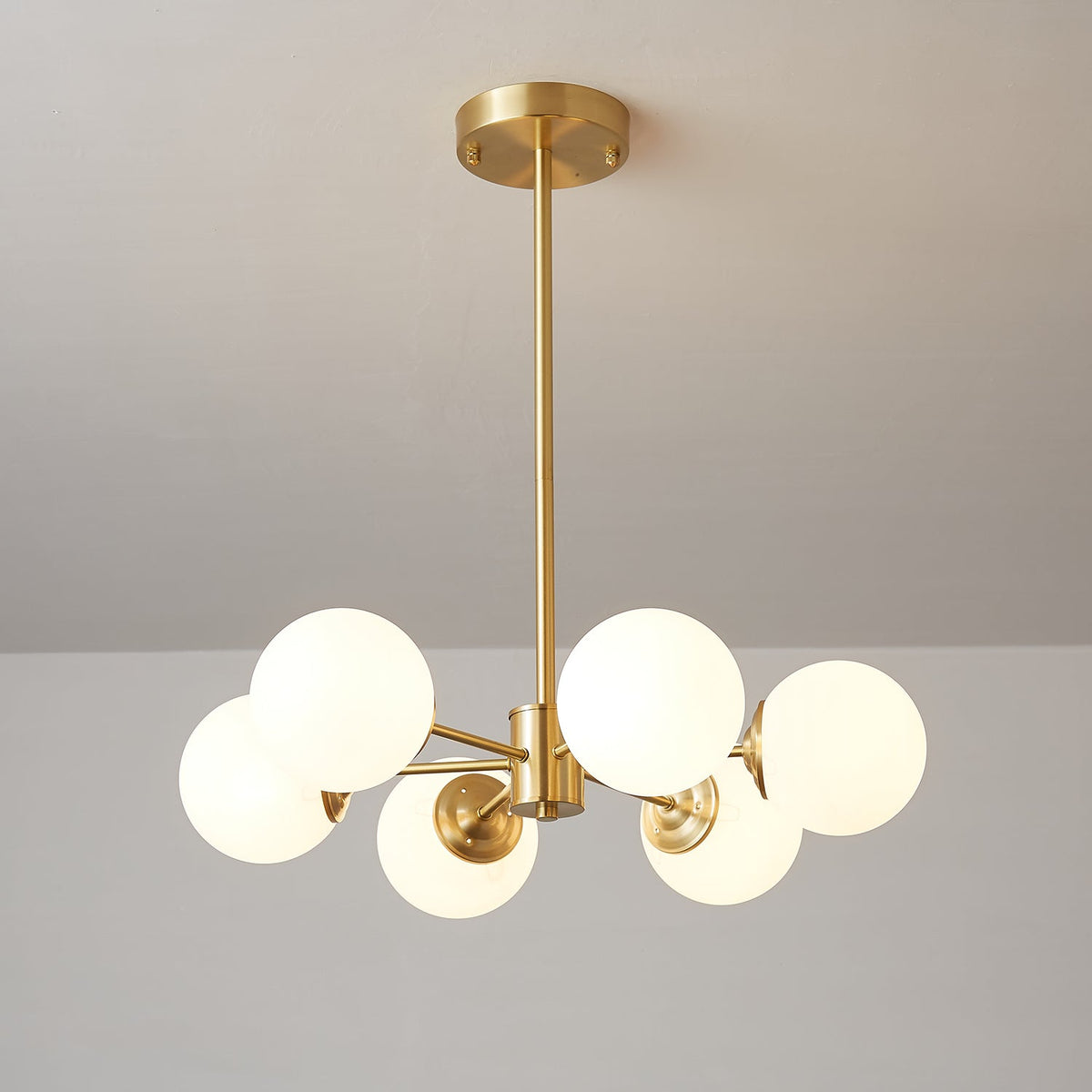 A Clérachic chandelier with six lit orbs on short brass arms, seen from a low angle with its canopy above.