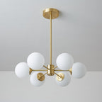 Unlit Clérachic chandelier with six matt white orbs on slim brass arms against a pale grey ceiling.