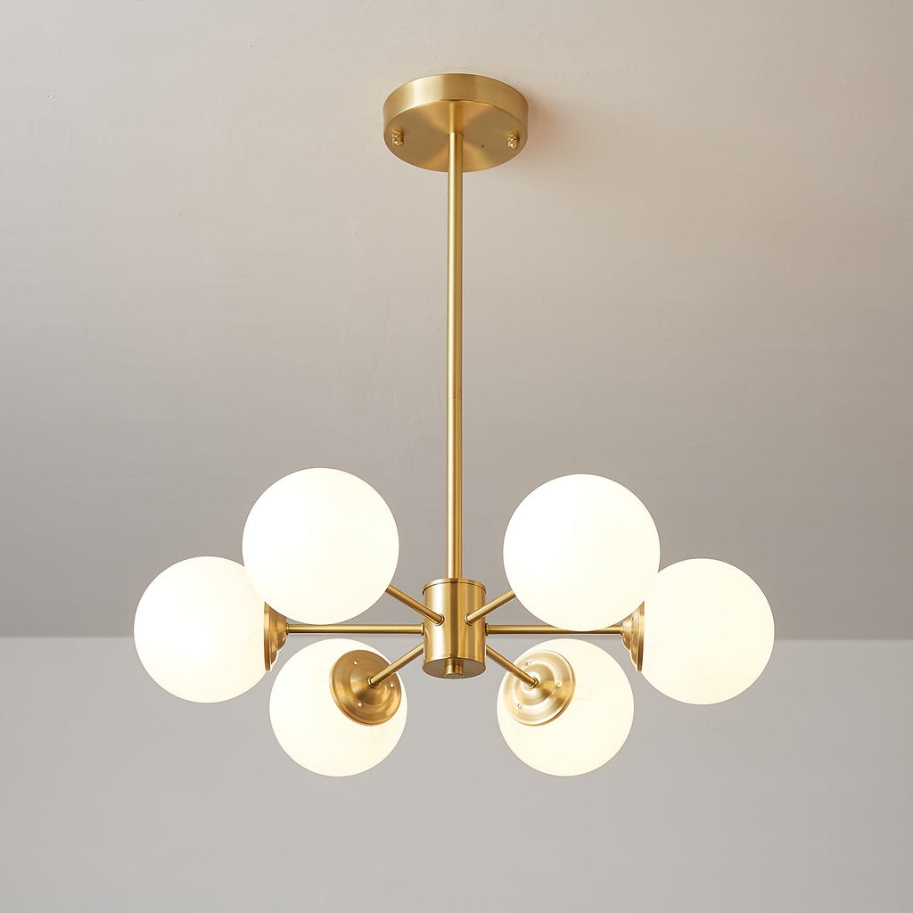 Six-orb Clérachic chandelier with warm-glowing frosted glass, centred on its brass stem on a taupe wall.