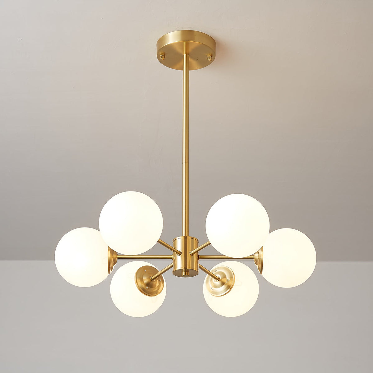 Six-orb Clérachic chandelier with warm-glowing frosted glass, centred on its brass stem on a taupe wall.