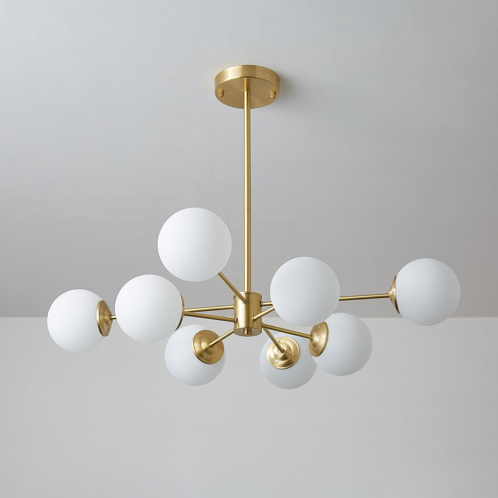 Unlit Clérachic chandelier with matt white orbs on brass arms, shown from below against a cool grey wall.
