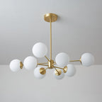 Unlit Clérachic chandelier with matt white orbs on brass arms, shown from below against a cool grey wall.