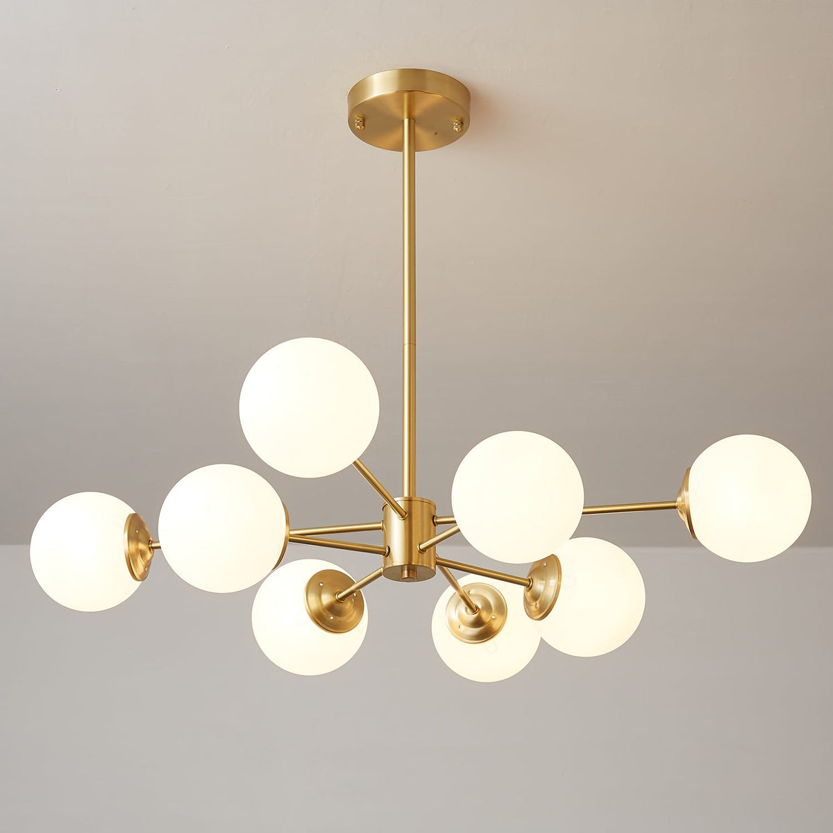 Clérachic chandelier with lit white orbs on brass arms of different lengths, hanging from a slim rod.