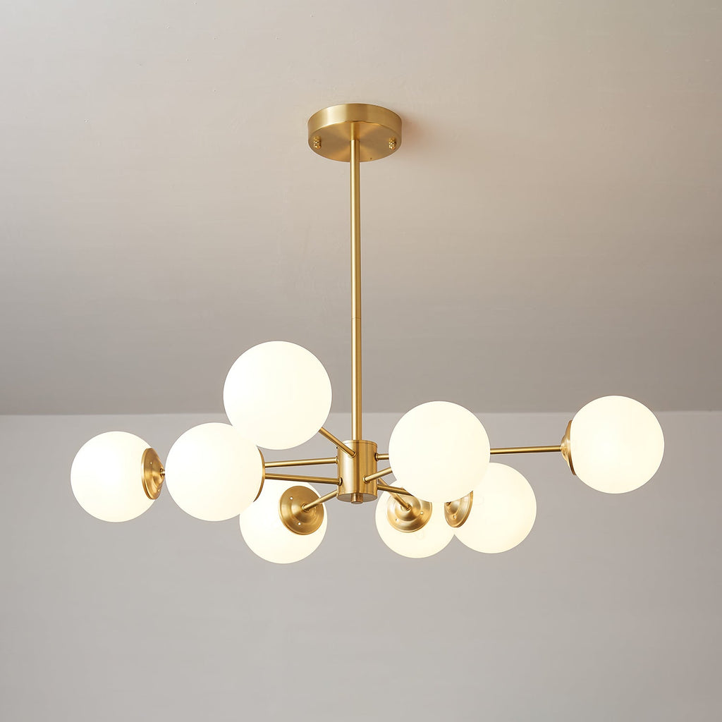 A Clérachic chandelier with lit frosted orbs on uneven brass arms, one globe set high on the left.