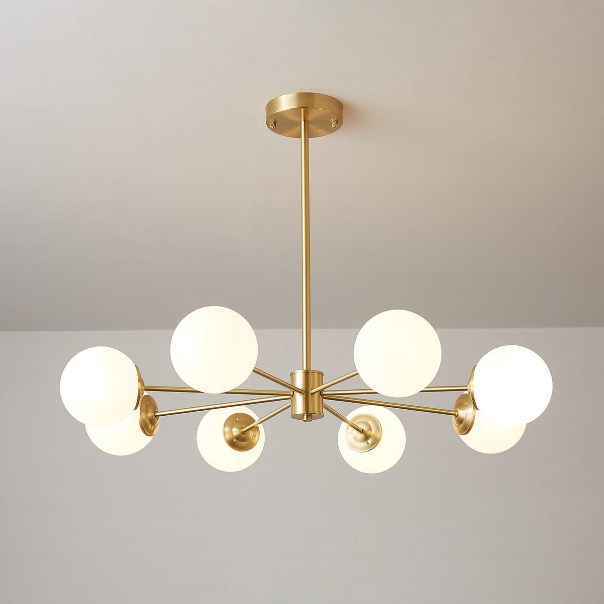 Eight lit white orbs fanned across a brass hub, a Clérachic chandelier with a slim drop rod.