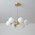 Unlit Clérachic chandelier with larger matt white orbs on short brass arms, against a cool grey wall.