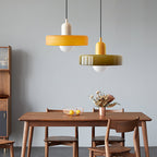Against a soft blue-grey wall above a walnut dining table, an orange disc pendant and an olive-green one hang at different heights, from Clérachic.