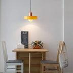 Above a small wooden table with white chairs and a gelato menu board, an orange disc pendant with a pink cap glows softly, from Clérachic.